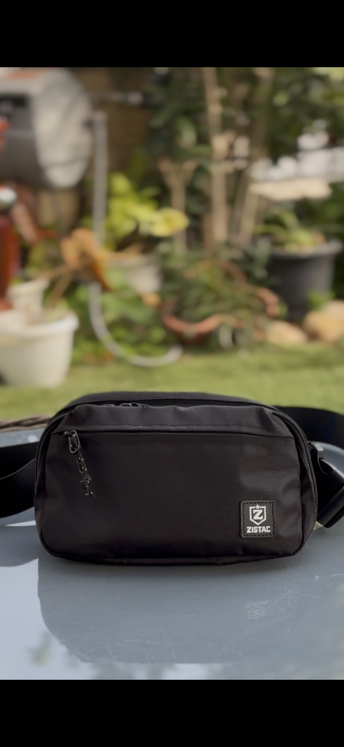Black waist bag on a reflective surface with a blurred garden background
